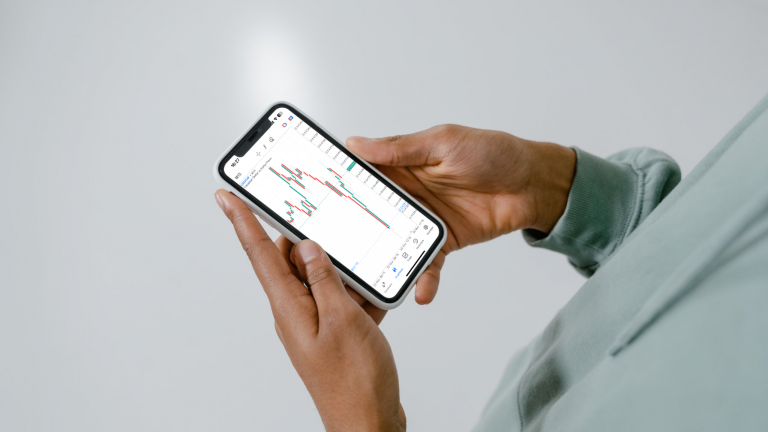 Main tenant un smartphone affichant un graphique de trading en temps réel, illustrant la synchronisation automatique des positions des traders Swapclub