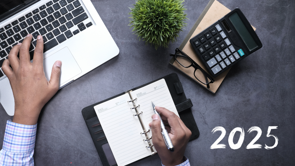 Photo d’un bureau de travail avec un ordinateur portable, un carnet de notes, une calculatrice et une main écrivant l’année 2025, illustrant la planification financière et l’analyse des opportunités de marché