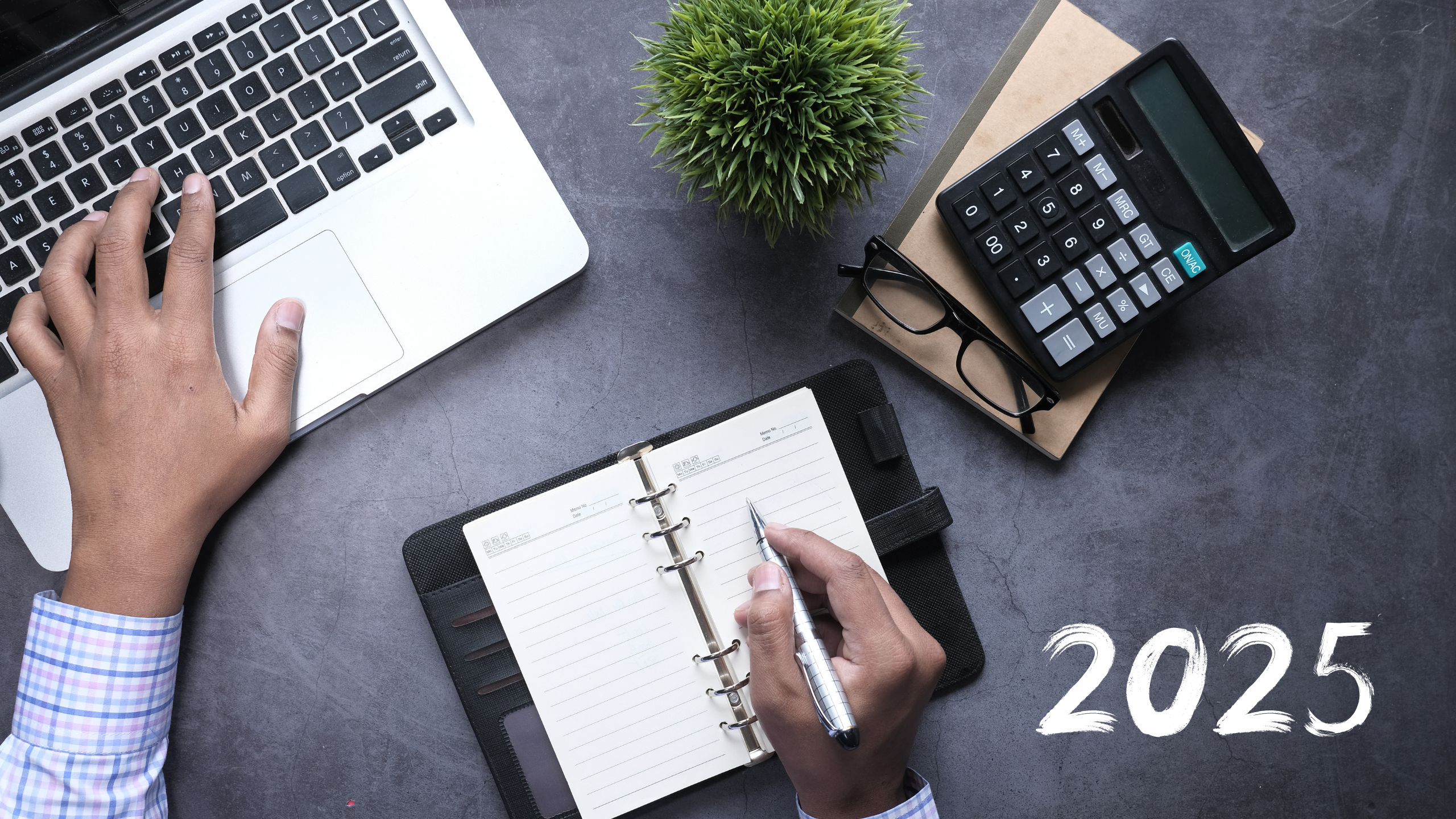 Photo d’un bureau de travail avec un ordinateur portable, un carnet de notes, une calculatrice et une main écrivant l’année 2025, illustrant la planification financière et l’analyse des opportunités de marché